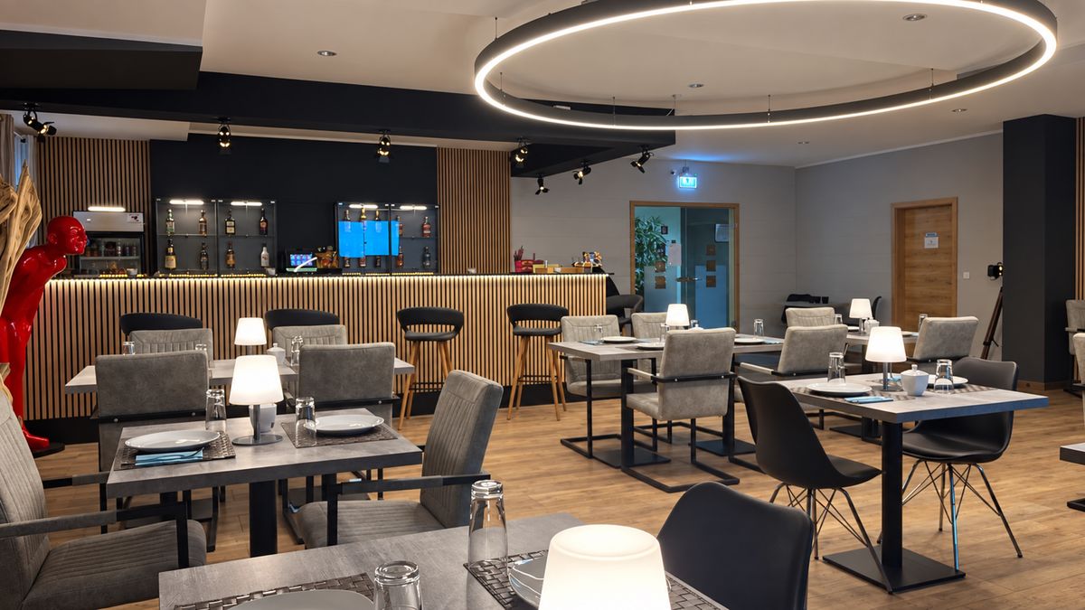 Frühstücksraum des Hotels mit gedeckten Tischen, Tischlampen und Blick zur Bar