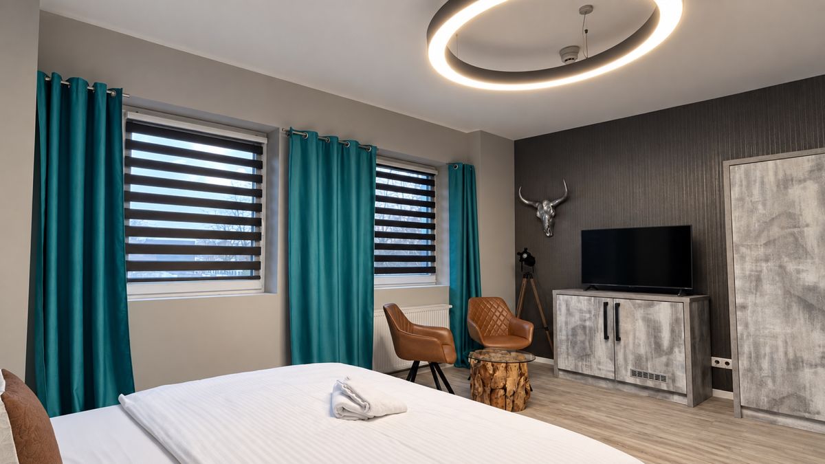 Doppelzimmer mit Bett, Sitzbereich am Fenster und türkisfarbenen Vorhängen